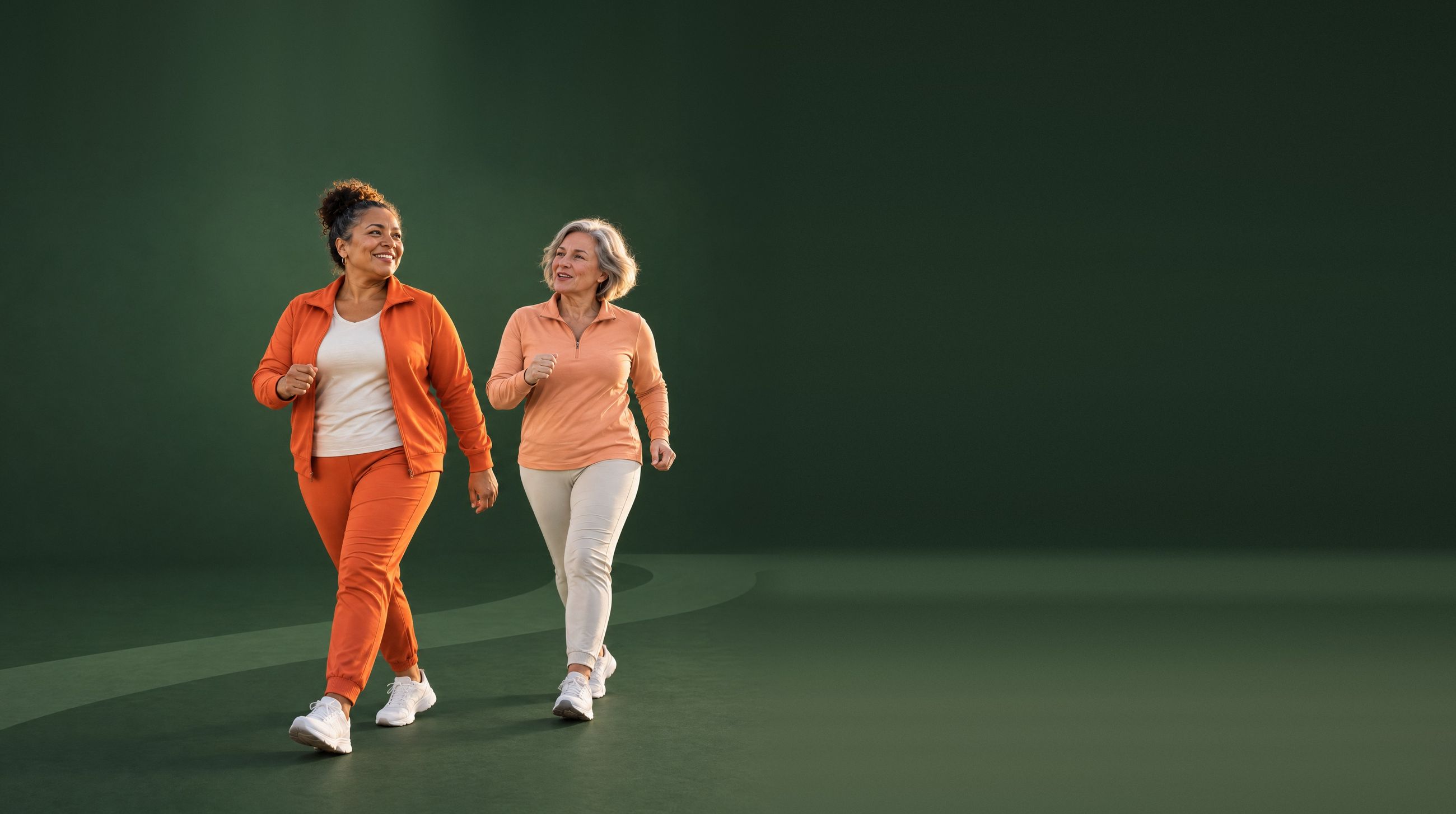 The same two friends in orange and apricot walking gear stride across a deep forest-green studio set.
